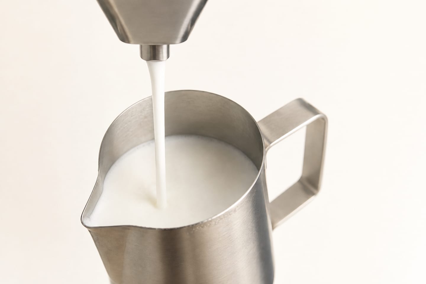 Textured milk pouring from a single steel spout into a pitcher, with no steam