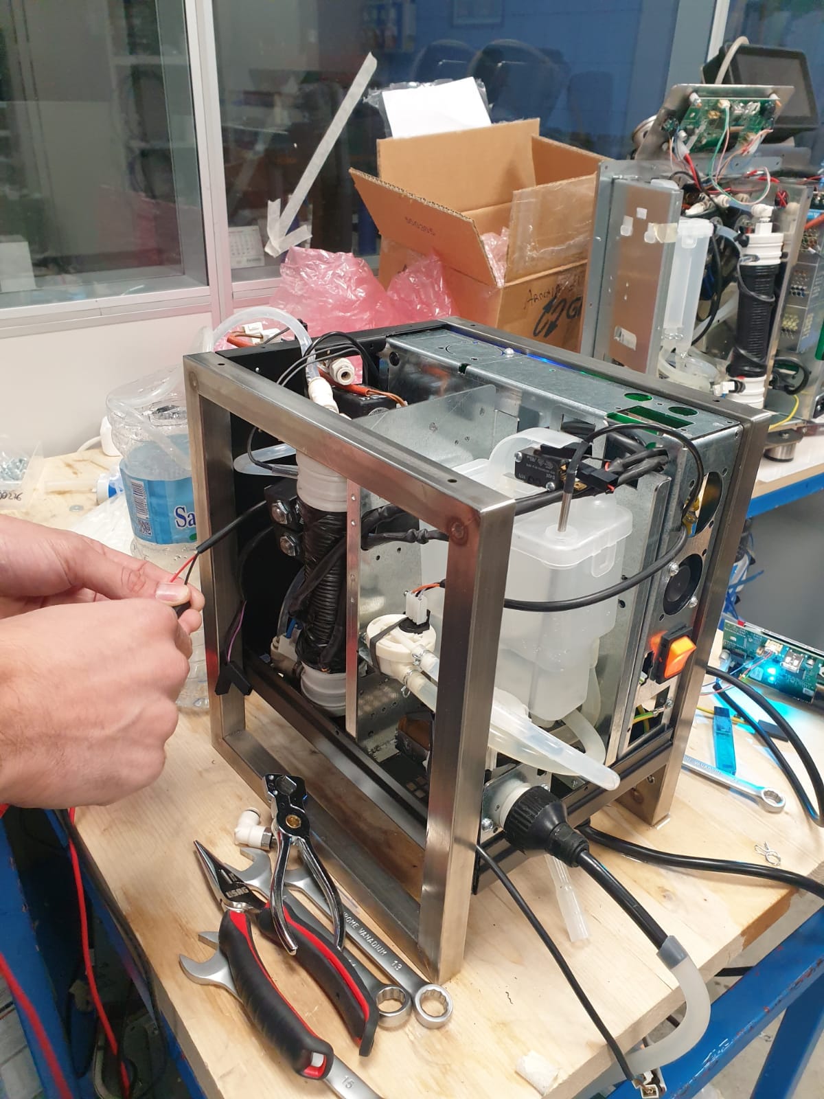 Early Heylo prototype chassis on a workbench, pump, tubing and wiring exposed, a technician adjusting a cable