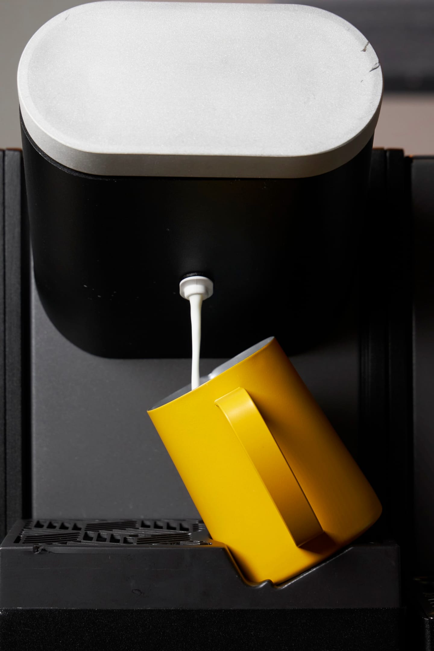 Heylo Milk Unit dispensing head pouring textured milk into a yellow pitcher on the tilt jug support
