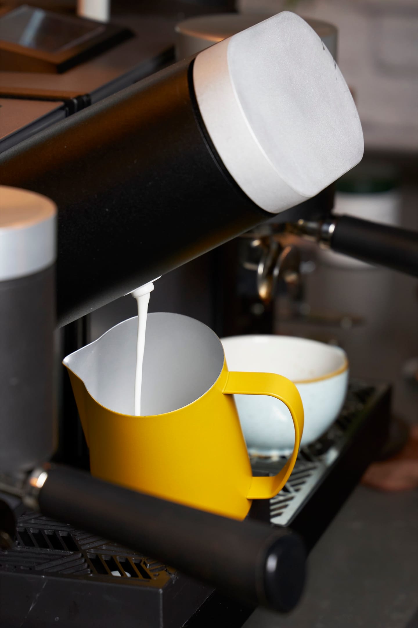 Heylo Milk Unit pouring textured milk into a pitcher, with the Heylo Coffee Unit beside it
